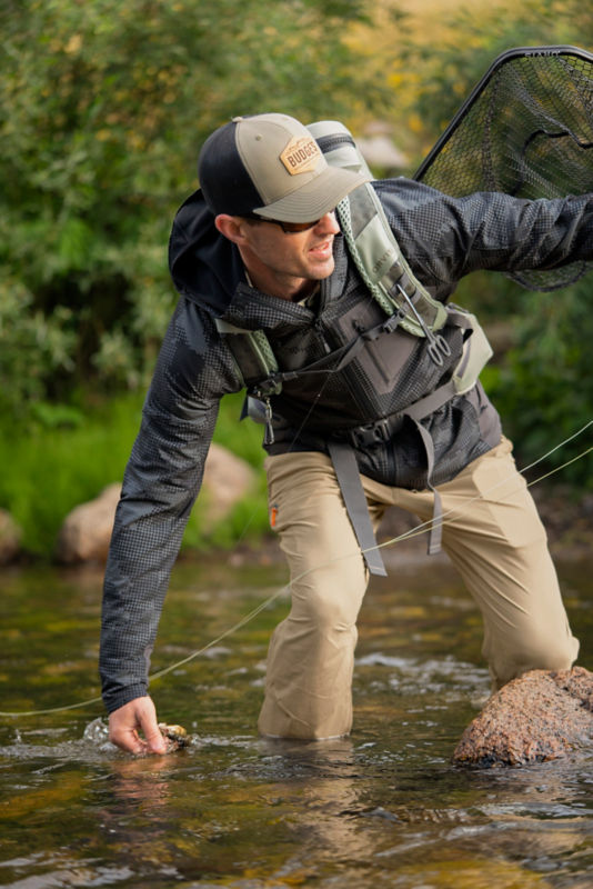 An angler navigates rocks and water to wade in a river.