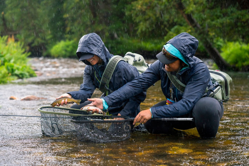 Anglers hold their catch in the middle of a river during the rain.