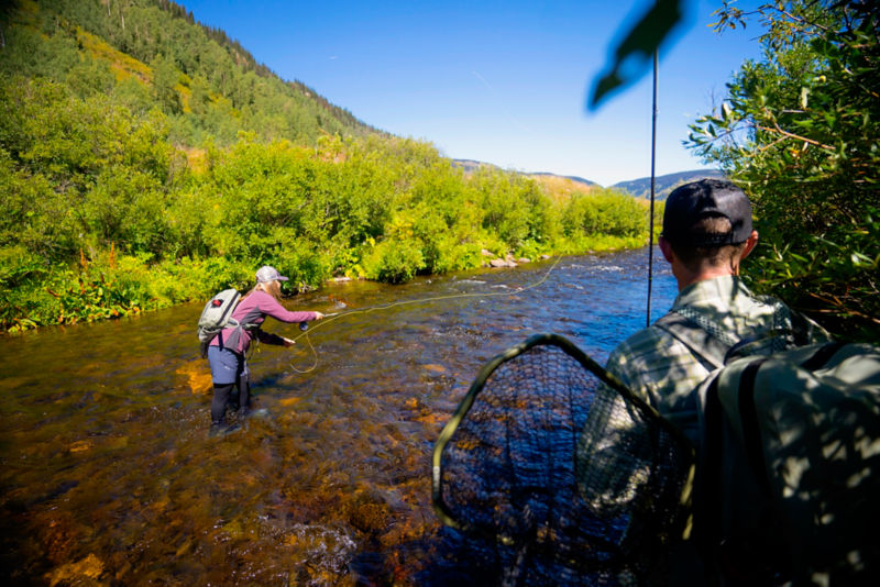 An angler in a Women's PRO LT Softshell Pullover tosses line in a rocky river.
