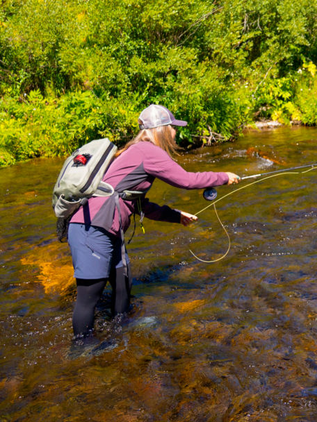 An angler in a Women's PRO LT Softshell Pullover tosses line in a rocky river.