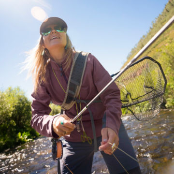 Woman angler casts in rocky river.