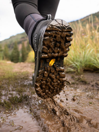 An angler in leggings lifts a boot out of the dripping mud.