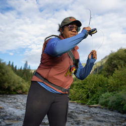 A woman wearing a PRO Sun Hoodie casting in a river