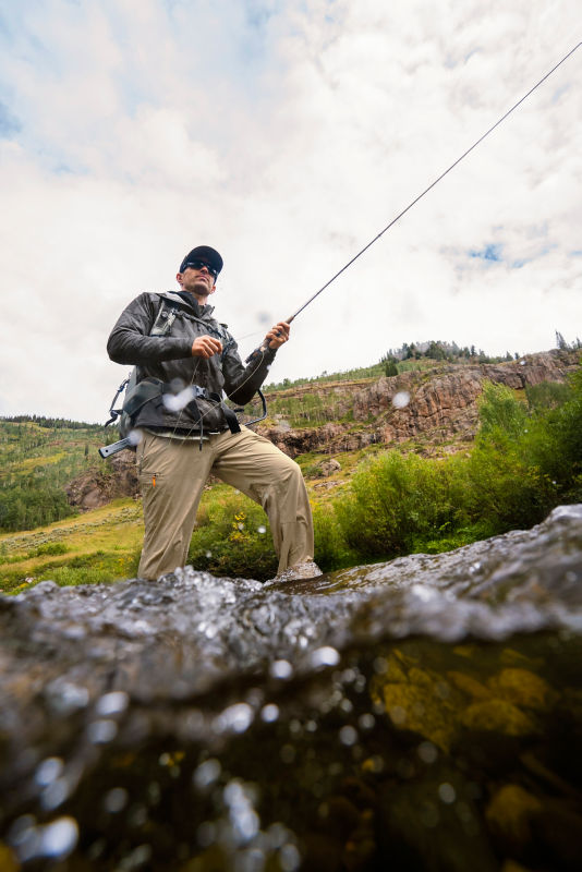 An angler in sunglasses steps through choppy waters on a gray sky day.
