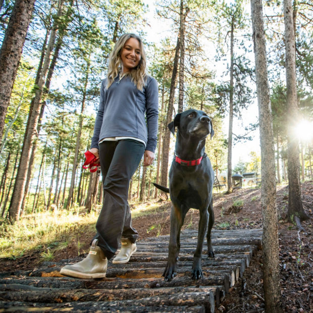 A woman and her black dog outside walking down wooden steps in the woods