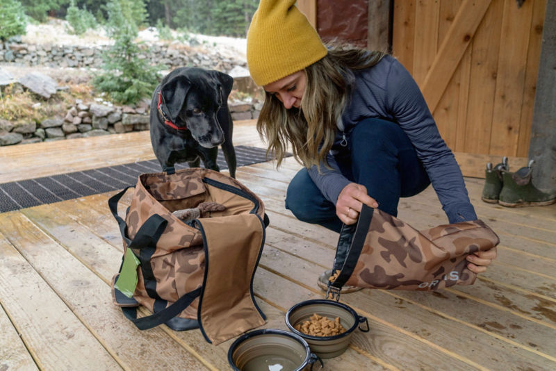 A woman feeding her black dog from a camo chuckwagon.