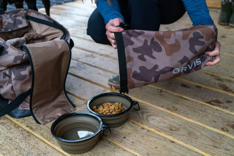 A closeup of a woman pouring food into a travel bowl from the camo chuckwagon.