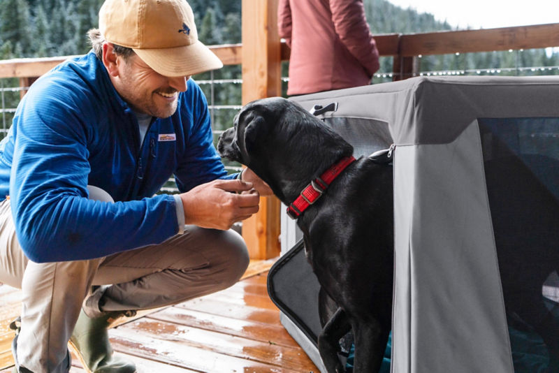 A person squats next to a collapsible cloth crate with a dog inside.