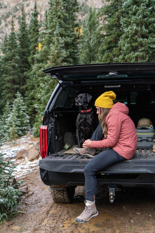 A woman sits on the tailgate of a truck with her dog.
