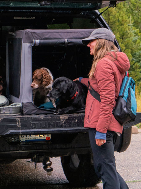 Two dogs laying in a large travel crate on truck bed with a woman petting them