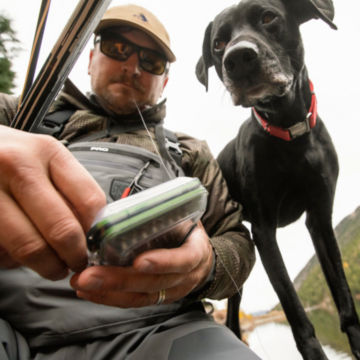 Man adjusts his angling accessories with his dog.