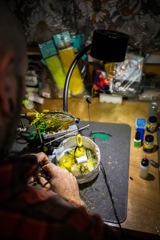 Two hands piecing a fly together at a table full of materials.