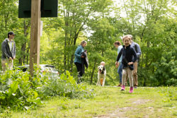 A girl runs ahead of a group down a green trail with dogs.