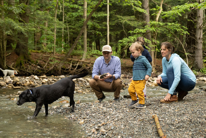 A family playing with their black Labrador Retriever on a rocky beach by a river