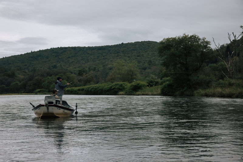 An angler casts from a boat on the river.