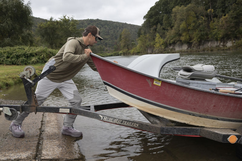 An angler in waders pushes a boat off of a trailer into the water.