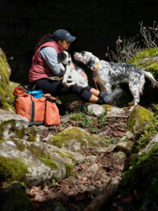 A woman crouching down in mossy woods next to her two dogs