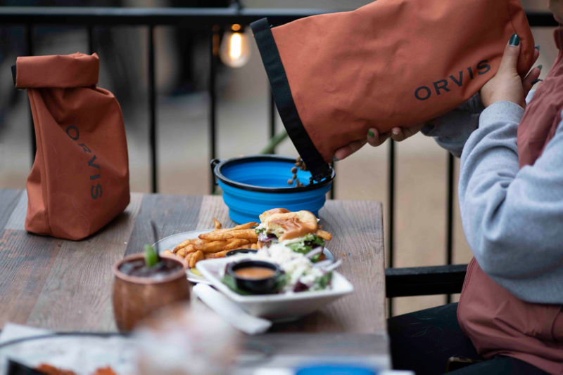 Dog food being poured out of an orange travel container into a blue travel bowl