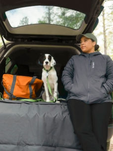 A woman and her dog at the back of a car in the woods