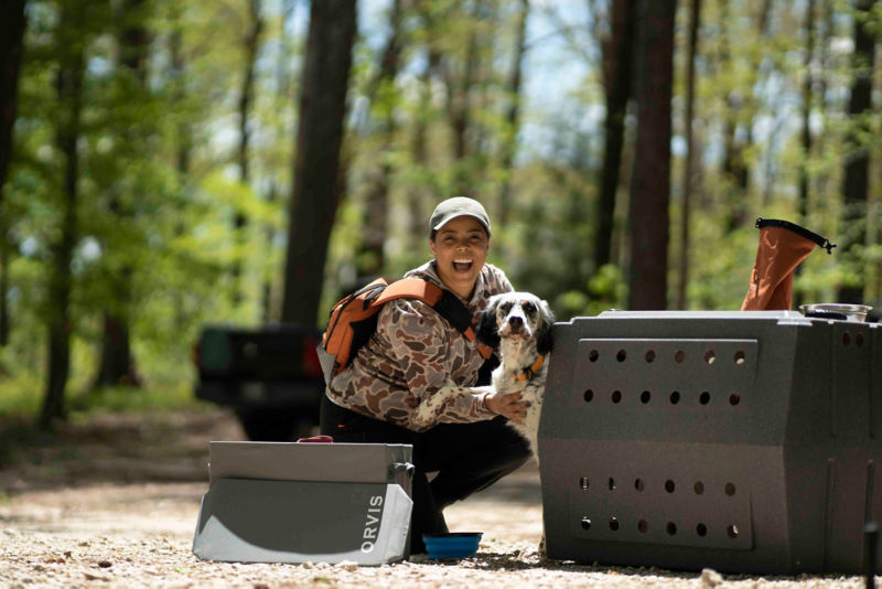 A smiling woman crouching down next to her dog in the woods