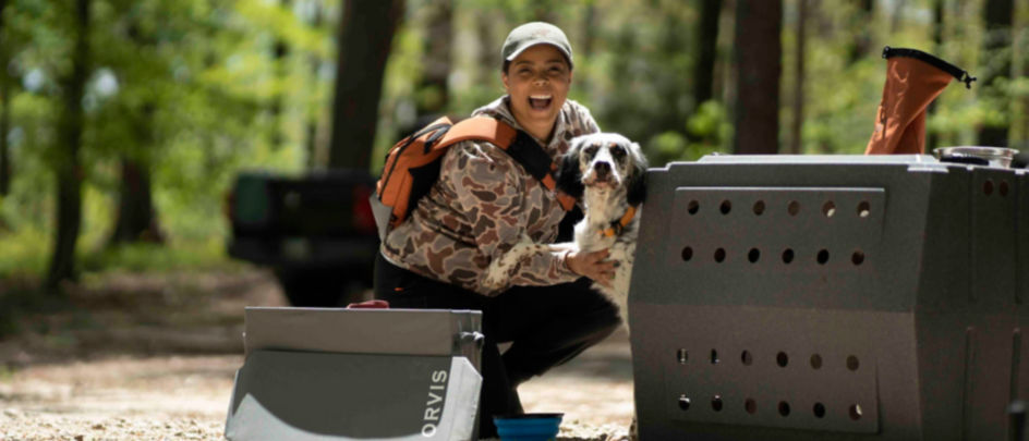A smiling woman crouching down next to her dog in the woods