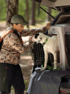 A woman helping her dog get into a travel crate