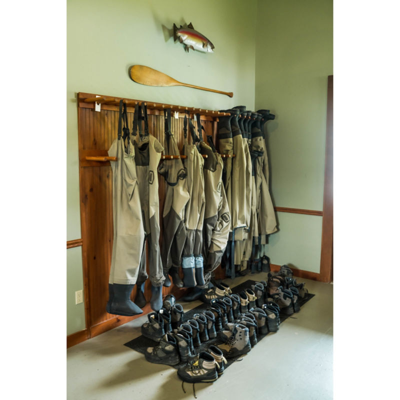 Waders hanging along a wall with wading boots lined up on the floor.