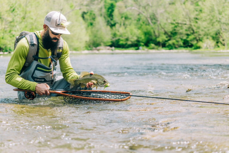 An angler kneeling in the river holds a fish above their net