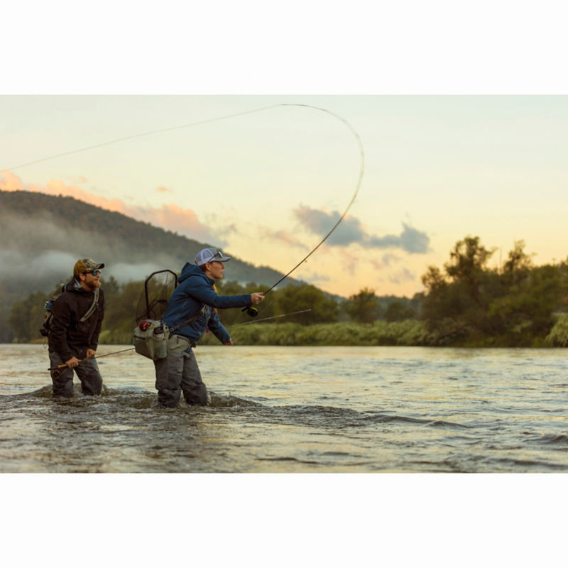 An angler watches another cast her rod from knee-deep in a wide river
