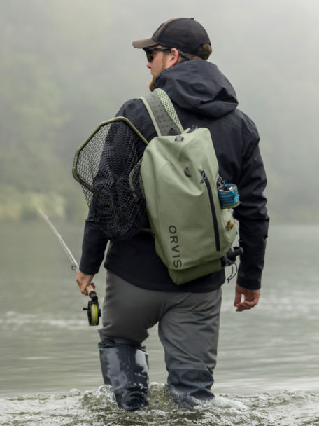Angler wearing PRO Waterproof Sling 14L wades through river.
