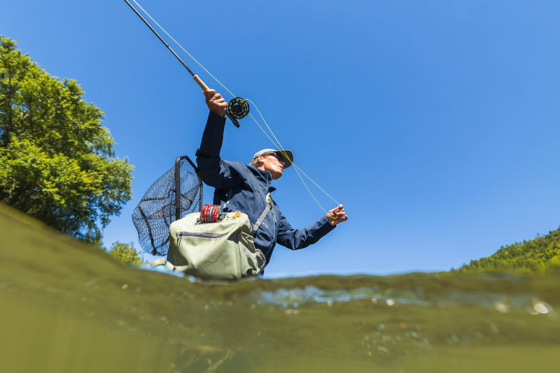 An angler mends her line silhouetted against a bright blue sky.