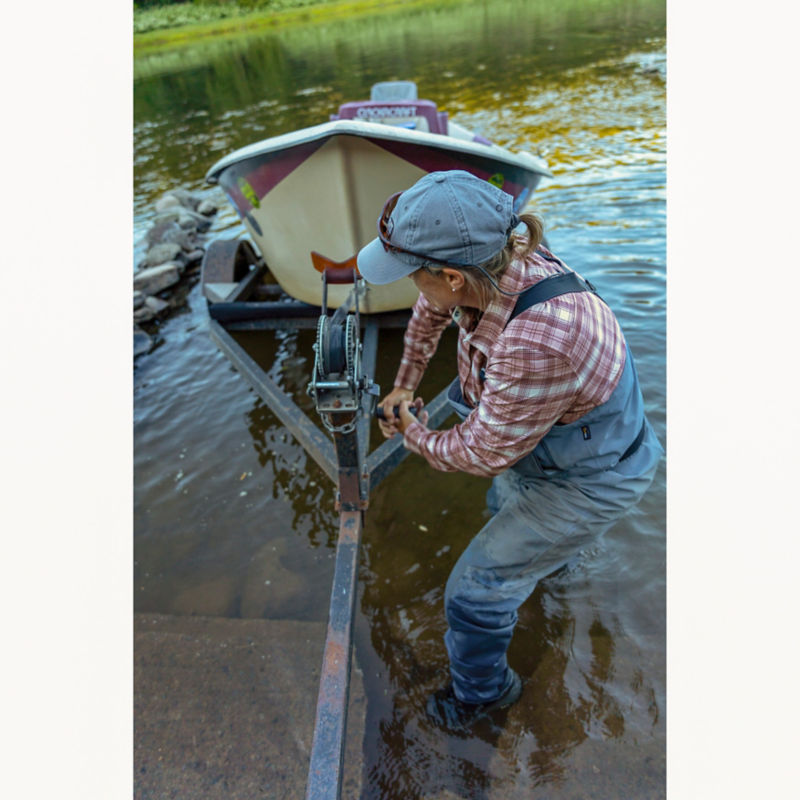 A woman in waders pulls her boat onto the boat trailer