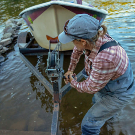 A woman in waders pulls her boat onto the boat trailer
