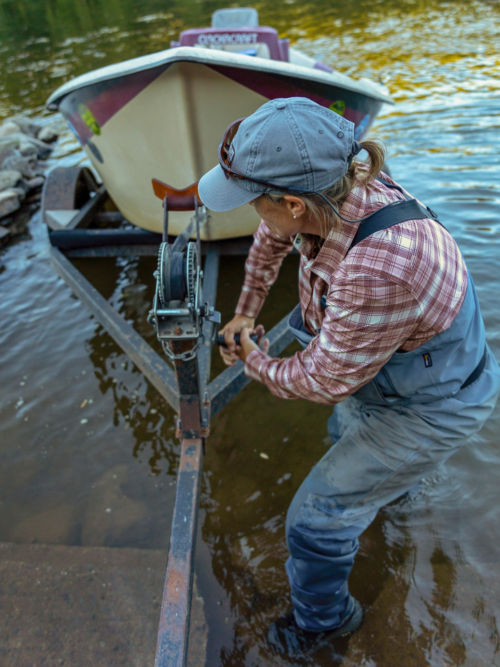 An angler lowers her skiff into a stream.