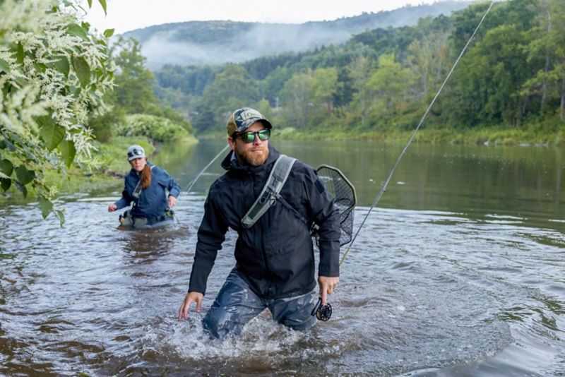 Two people wearing waders, walking in a swift moving river.