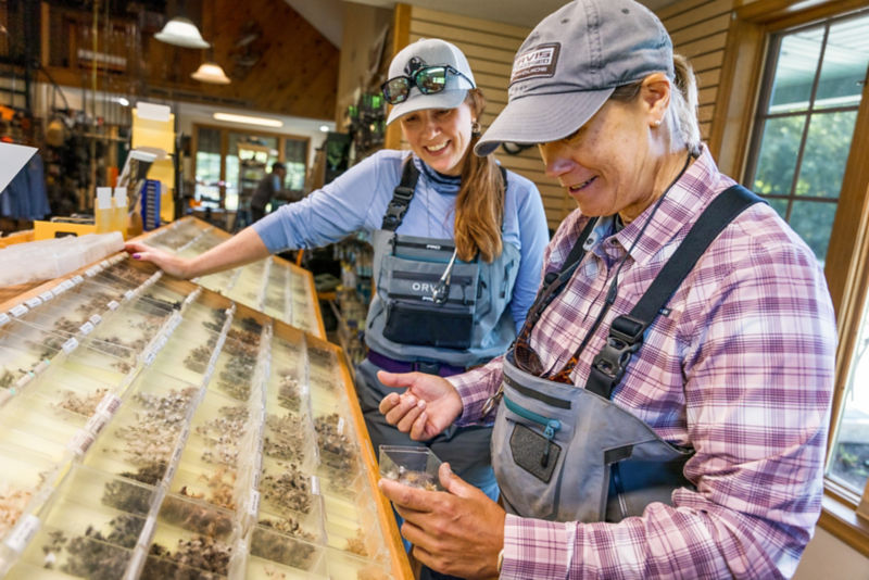 Two women in waders pick through a display of flies.