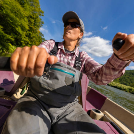 An angler rows a boat under a bright blue sky
