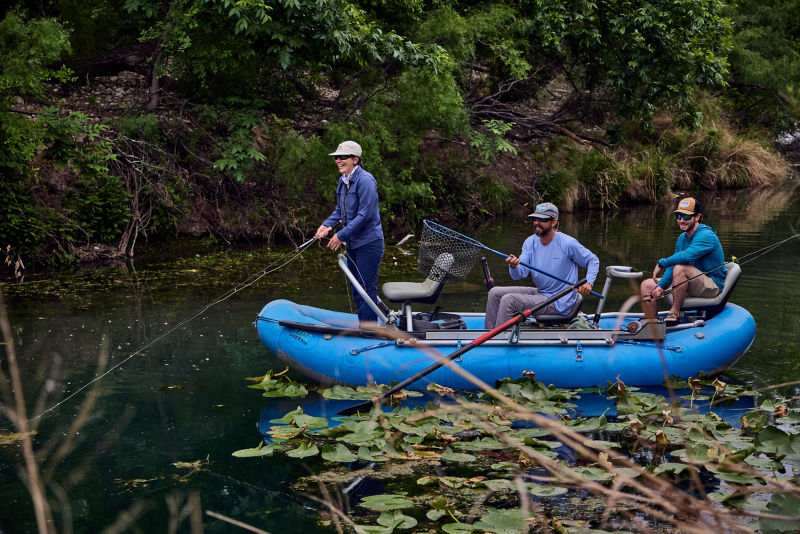 A raft full of anglers floats through greenery.