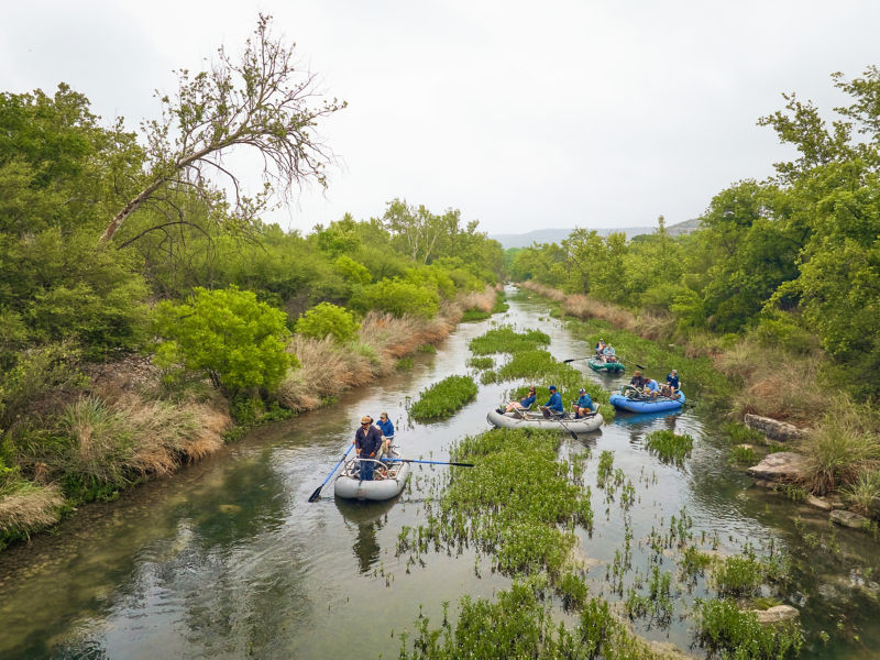 Four rafts of anglers make their way down a shallow river.