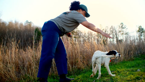 A woman teaching her dog to spin outside in a field