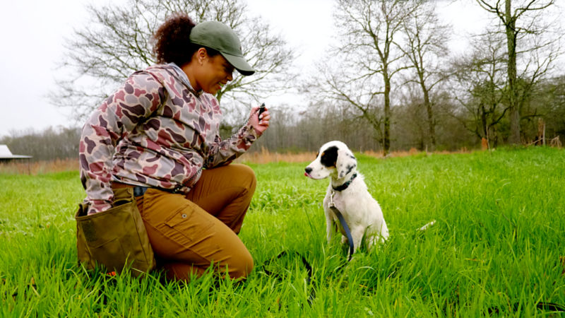 A woman kneeling on the grass next to her puppy.