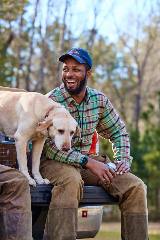 A smiling man sitting on the back of a truck bed next to his yellow lab.