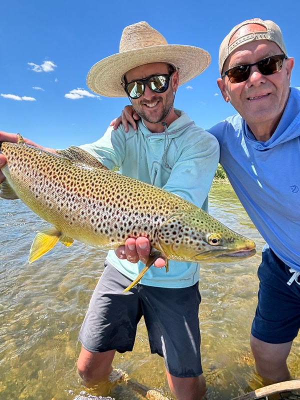 Two people show off a giant spotted fish under a blue sky.