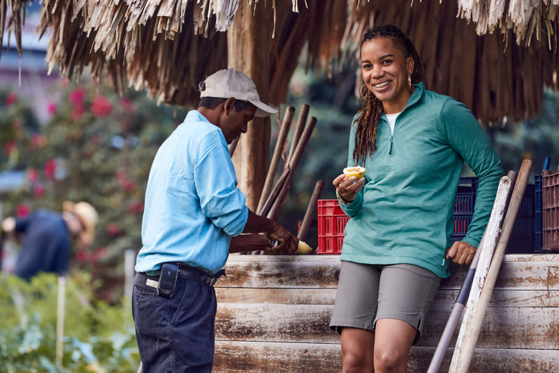 Woman standing under a palm roof eating fruit.