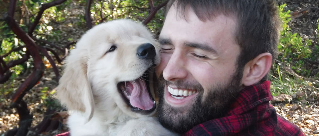 A smiling man snuggles a golden puppy.