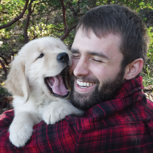 A man wearing buffalo check snuggling with a golden puppy.