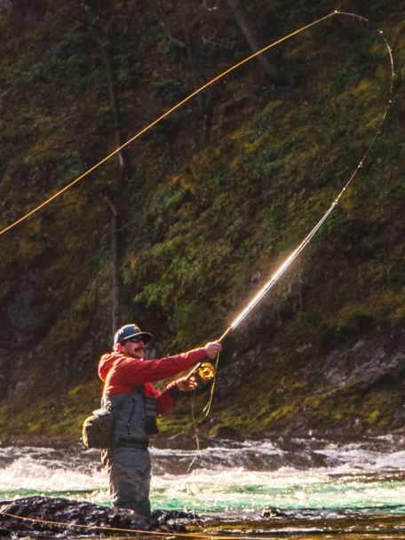 Man throws line downstream as he wades over a rocky river.
