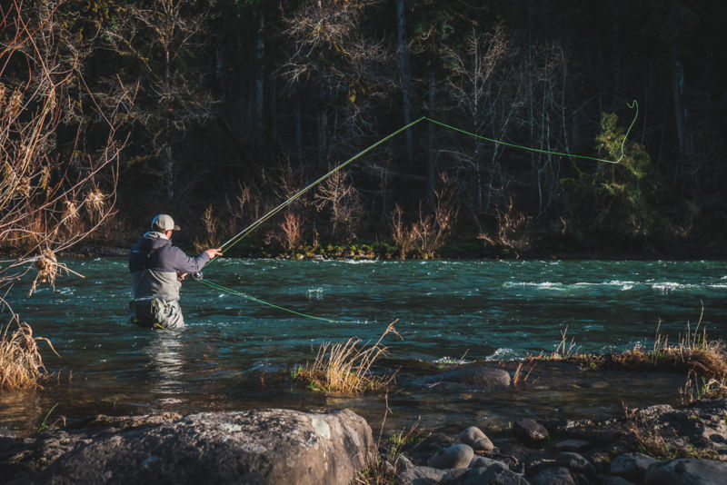 An angler wades waist-deep in a shallower spot of a deep river.