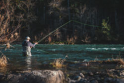 An angler wades waist-deep in a shallower spot of a deep river.