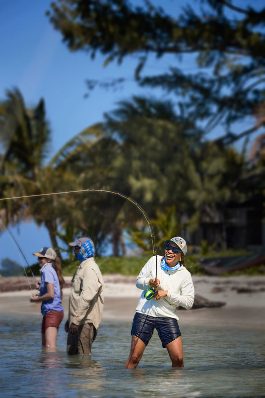 Several anglers smile while knee-deep in the ocean fly fish in the tropics.